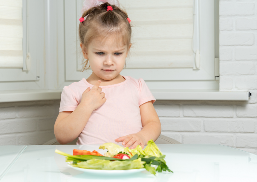 Alimentation enfants végétarisme: une fillette regarde une assiette de légumes.