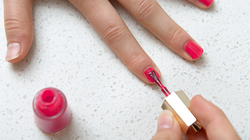 Une main de femme applique du vernis à ongles rose sur la main gauche.