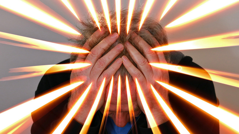 Kopfschmerzen, Spannungskopfschmerzen, Schmerzmittel: jemand stütz den Kopf auf die Hände, Lichtstrahlen überall