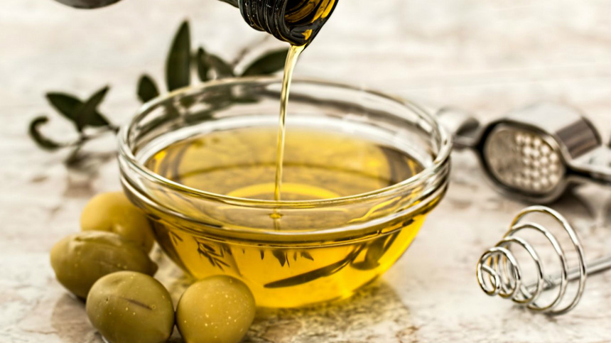 Ernährung, Öle, Fette: Eine Ölflasche, die in eine mit Öl gefüllte Schüssel tropft, mit ein paar Oliven daneben