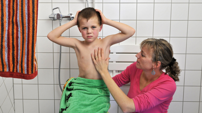 Tiques piqûres réaction: une maman examine son garçon qui a les bras levés.