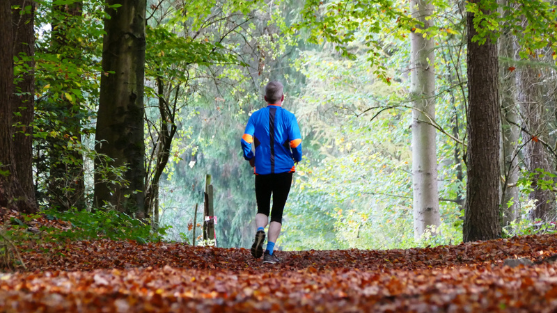 Un homme court sur un chemin couvert de feuilles mortes. On le voit depuis l'arrière.