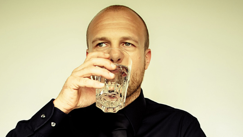 Ein Mann trinkt aus einem Glas Wasser.