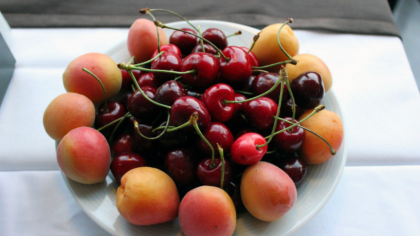 Eine weisse Schüssel mit Aprikosen und Kirschen steht auf einer weissen Tischdecke