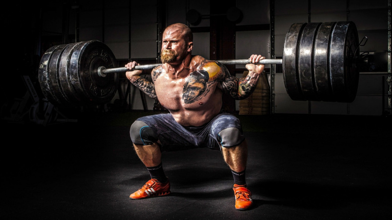 Un homme tatoué soulève des poids.
