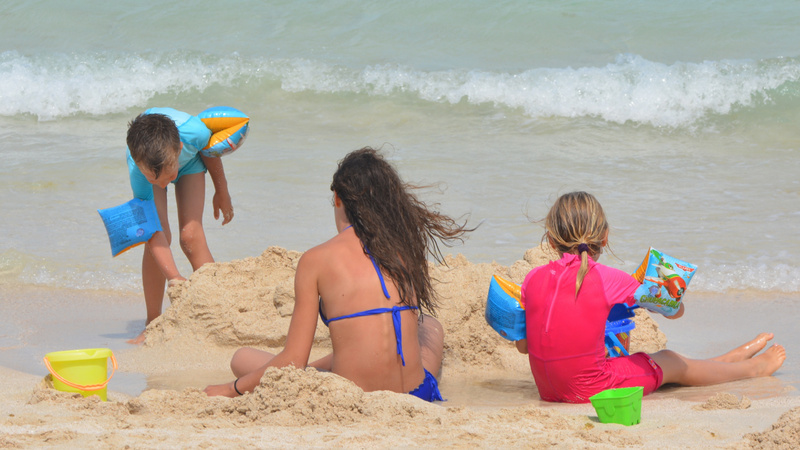 Noyades conseils surveillance enfants: une femme et deux enfants vus de dos dans le sable d'une plage.