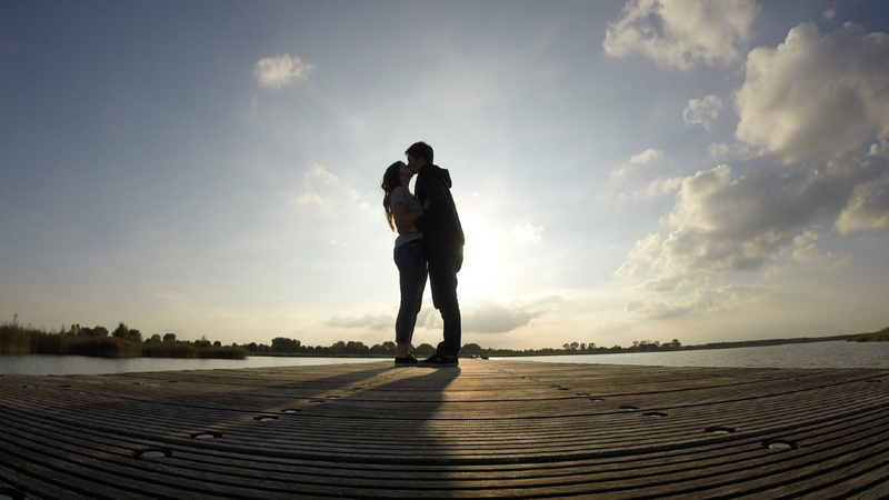 Un couple au bord de l'eau le soir. Ils s'embrassent.