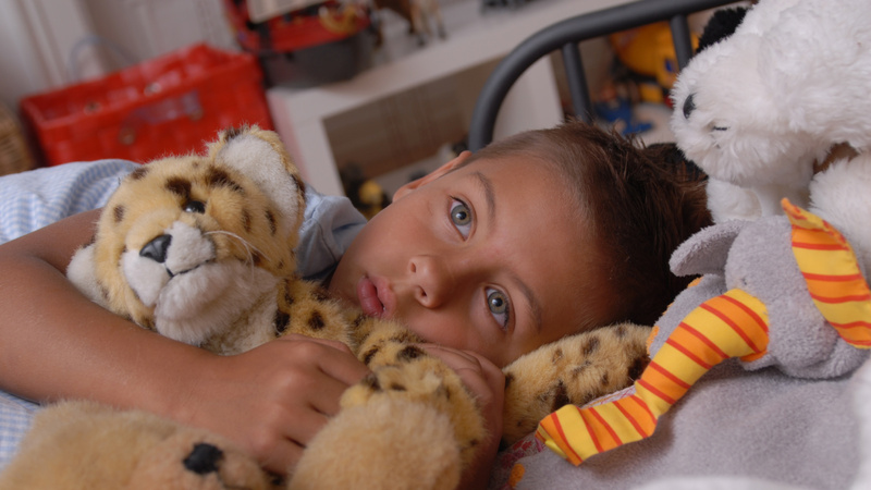 Médecine naturelle thérapie spagyrie: Une petite fille est couchée dans son lit et serre des peluches contre elle.