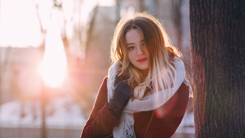 Eine junge Frau, dick eingepackt in einen Wintermantel und einen Schal, geniesst die Wintersonne