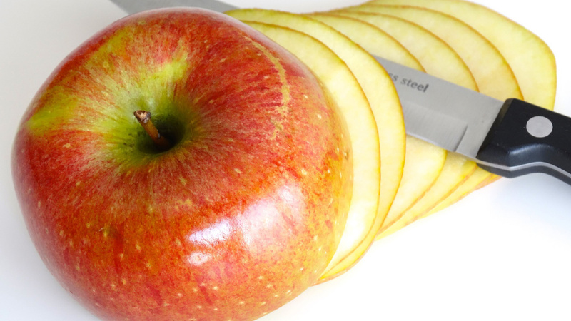 Une pomme coupée en fines tranches avec un couteau entre deux tranches.