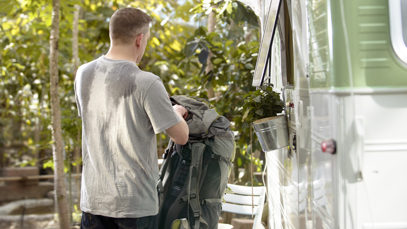 Schwitzen, Schweiss, Stinken: Mann in grauem T-Shirt von hinten, sein Rücken ist total verschwitzt. Er hat gerade seinen Rucksack abgelegt.