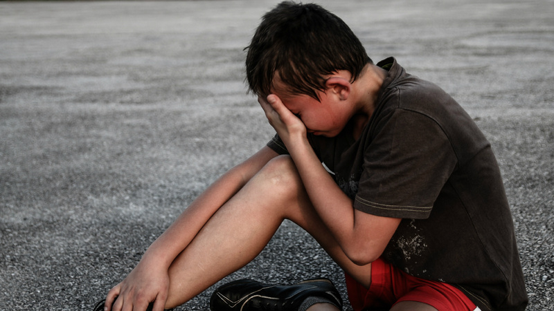 Un jeune homme est assis par terre. Il se tient le visage avec la main gauche.