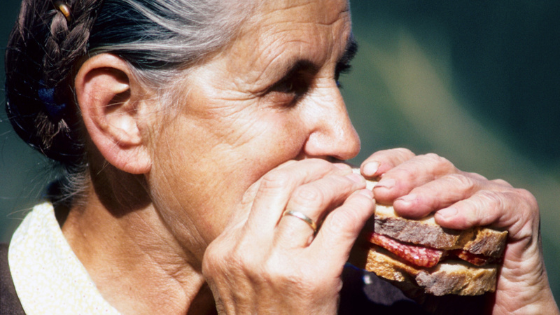 Une femme âgée mord dans un sandwich au salami.