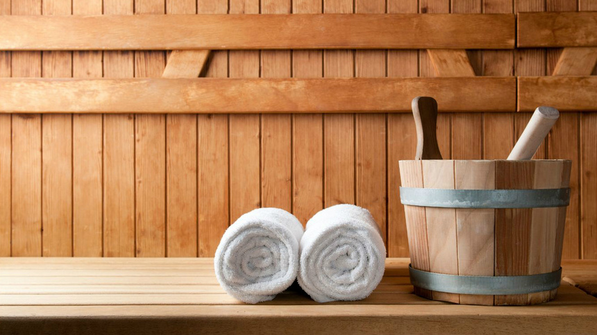 Wellness, Sauna, schwitzen: Holzsauna, ein hölzerner Bottich und daneben drei aufgerollte weisse Frotteetücher