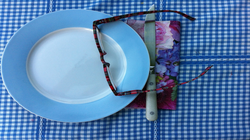 Ernährung, Fasten: Ein Porzellanteller, weiss mit blauem Rand, steht auf einer blau-weiss karierten Tischdecke, auf einer Papierserviette mit Blumenmotiv liegt ein Messer, auf dem Teller liegt eine Brille
