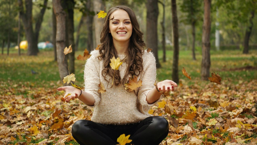 Une femme est assise en tailleur dans un parc dans des feuilles.