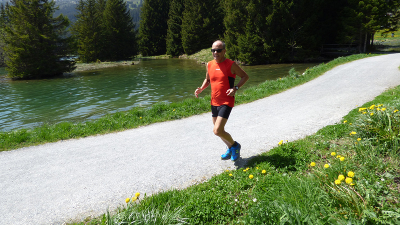 Un homme en maillot rouge court sur un chemin au bord d'un lac