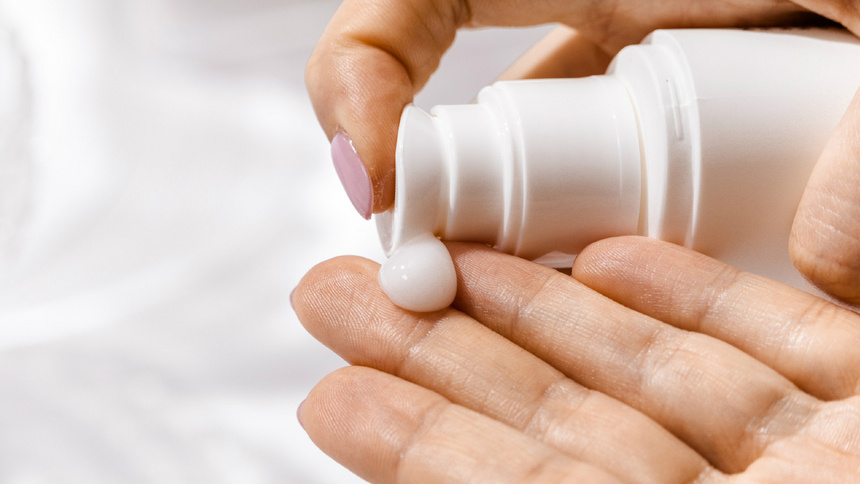 Une main de femme verse du produit de soins sur une autre main.