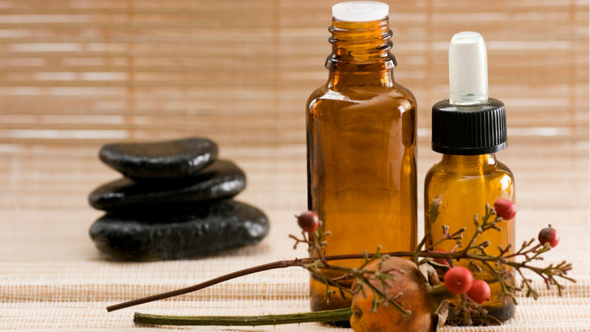 Un flacon d'huile de massage posé devant un bouquet et des pierres de massage