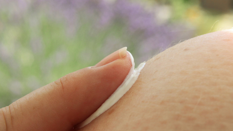 Schönheit, Pflege, Haut: Jemand trägt mit dem Zeigefinger Bodylotion auf.