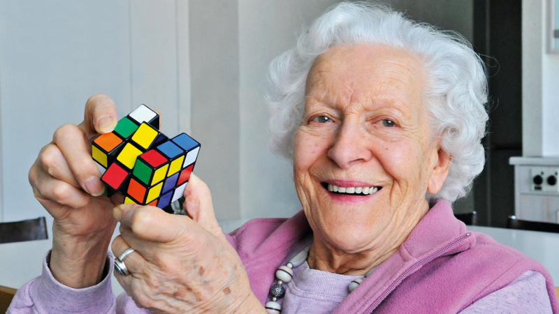 Une vieille dame s'amuse avec un Rubik's cube en souriant.
