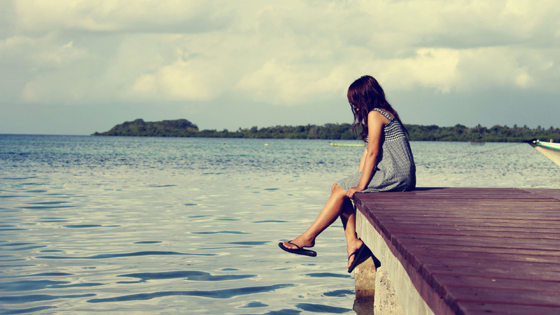 Une femme est assise sur une jetée et regade dans l'eau