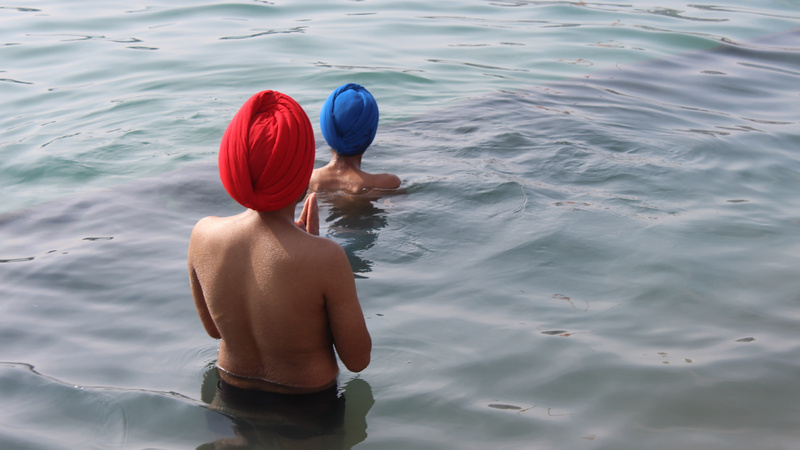 Schönheit, Baden, Wellness: Zwei indische Männer, einer mit einem roten, einer mit einem blauten Turban, tauchen ins Meer ein.