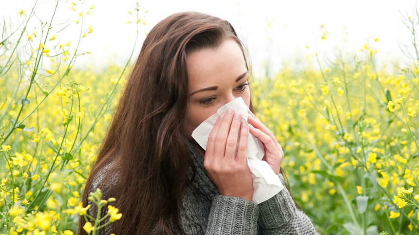 Allergie, Heuschnupfen, Pollenallergie: eine Frau, die sich auf einem Feld die Nase putzt