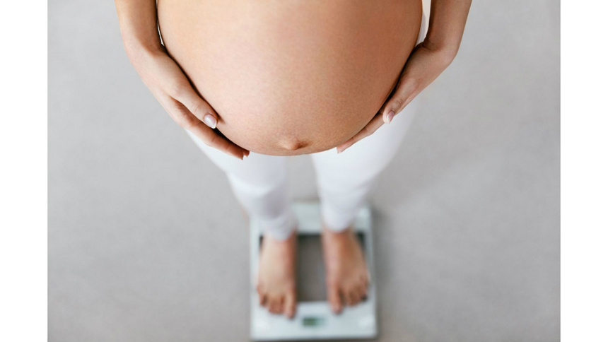 Schwangerschaft, Gewichtszunahme, Mutter: Eine schwangere Frau, die mit nacktem Bauch auf einer Waage steht