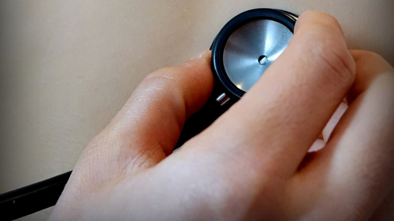 Une main de médecin pose un stéthoscope sur la peau d'un patient