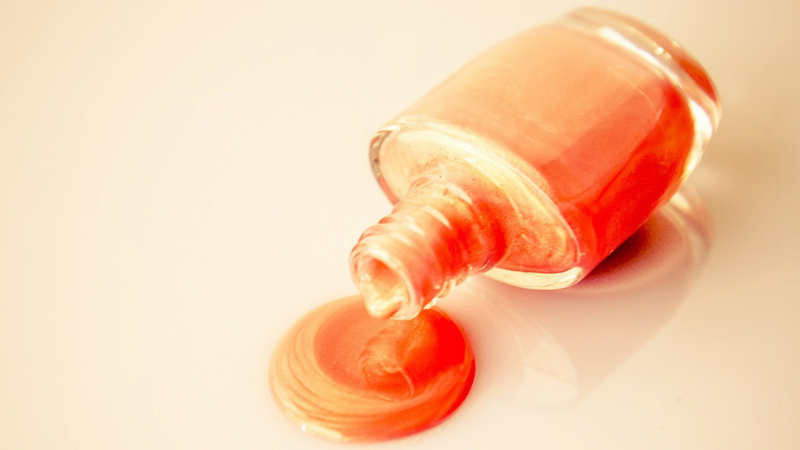 Schönheit, Pflege, Fuss, Nagellack: Fläschchen mit roséfarbenem Nagellack liegt auf der Seite, die Flasche ist offen und es fliesst Nagellack daraus auf den Tisch