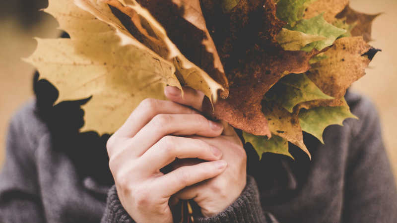 Ein Mann verdeckt sein Gesicht mit Laubblättern.