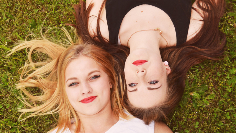 Zwei Frauen liegen im Gras. Eine blonde Frau und eine braunhaarige Frau.