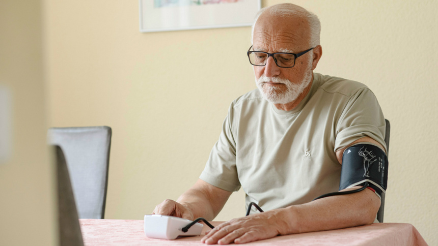 Un homme âgé est assis à une table et prend sa pression sanguine.