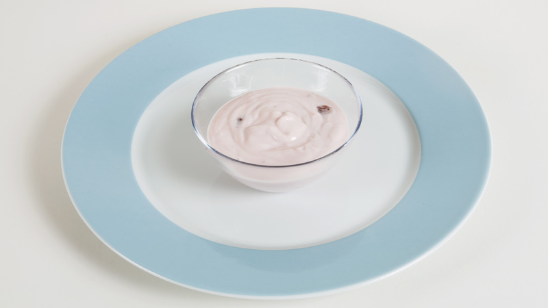 Un gobelet de yaourt aux fraises posé sur une assiette blanche avec un bord bleu clair