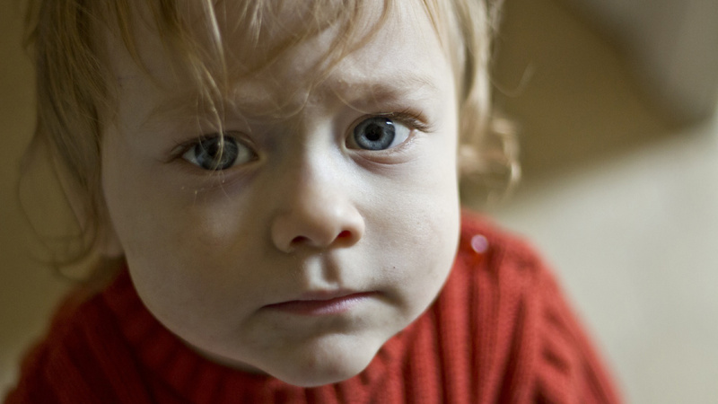 Blasenentzündung, Kinder, Antibiotika: Kleines Kind mit rotem Wollpullover und blonden Haaren schaut ängstlich in die Kamera
