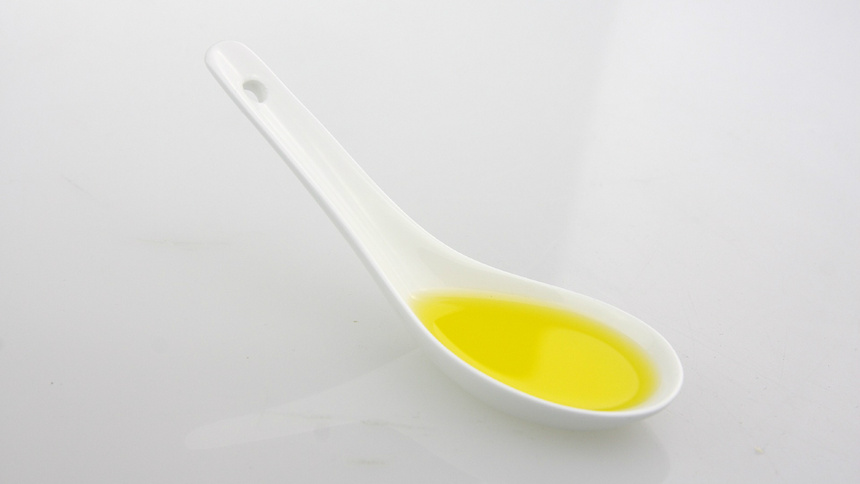 Ein weisser Löffel gefüllt mit einem gelben Öl auf weissem Untergrund