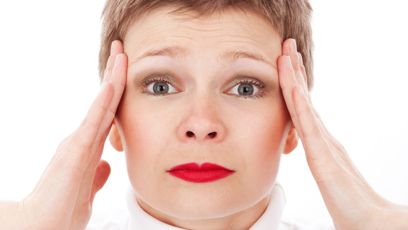 Une femme se tient les deux tempes. Elle a l'air d'avoir mal à la tête.