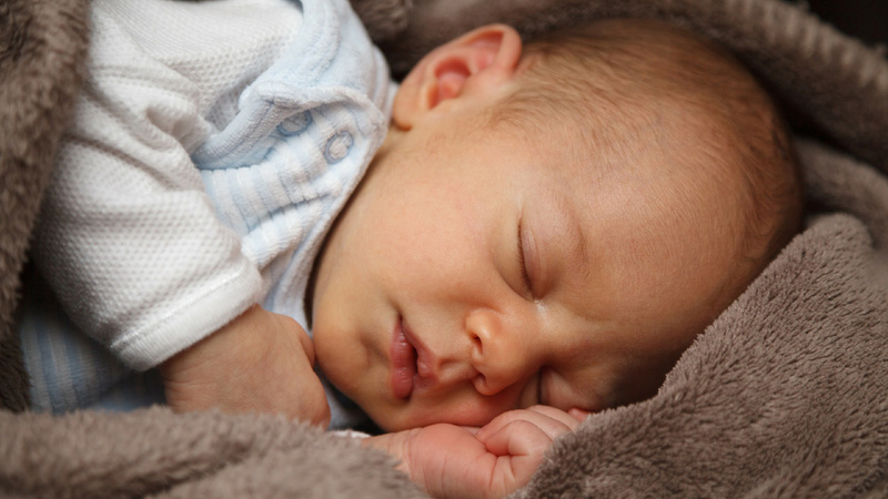 Un bébé dort paisiblement sur le côté dans une couverture brune.