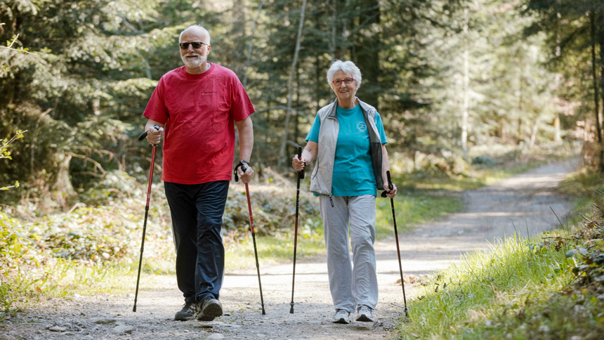 Alter, Bewegungsapparat, Gelenke, Muskeln: Ein alter Mann und eine alte Frau gehen mit Wanderstöcken einem Waldweg entlang.