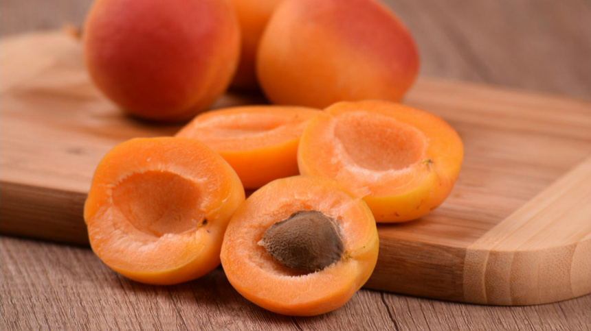 Ernährung, Mineralstoffe, Vitalstoffe: Auf einem weissen Porzellanteller liegen fünf Aprikosen, eine davon halbiert. Ein Rüstmesser liegt dabei, der Teller steht auf einem orangfarbenen Tischtuch