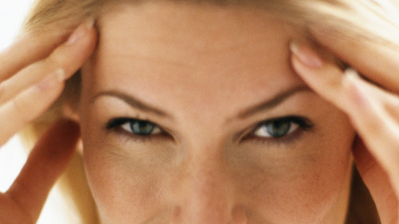 Le haut du visage d'une femme qui se tient les tempes avec les deux mains.