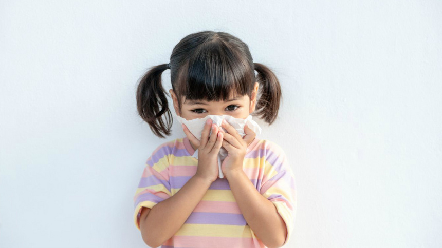 Une petite fille éternue dans un mouchoir.