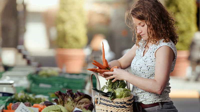 Une femme fait son marché. Elle achète des carottes.