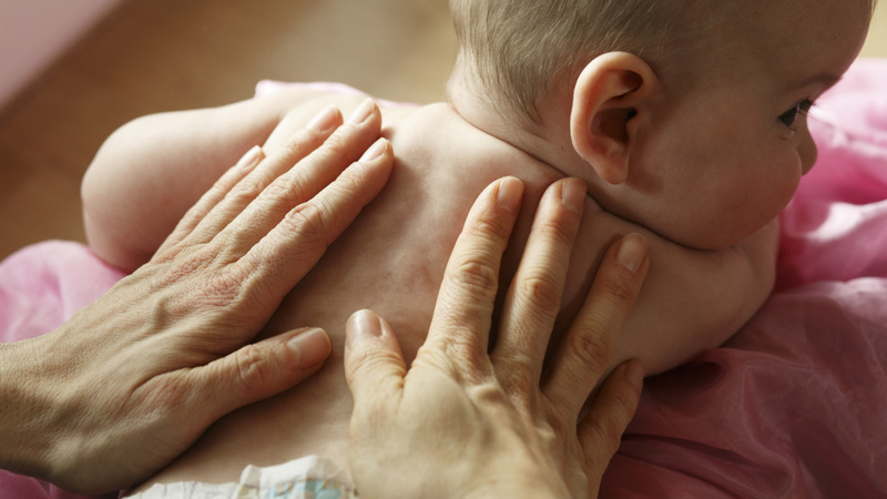 Un bébé est sur le ventre et sa maman a les mains posées sur son dos.