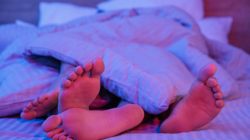 Verhütung, ein Paar im Bett, Hormone: Füße, die aus einem Bett herauswachsen