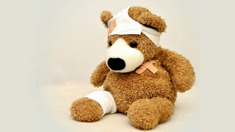 Tiere, erste Hilfe, Tierapotheke: Teddybär, Bein und Kopf verbunden, ausserdem ein Pflaster auf der Brust