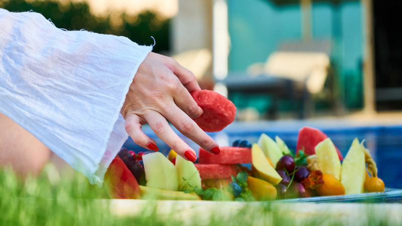 Ernährung, gesund, Tipps: Frau greift aus einer Schale mit geschnittenen Früchten ein Stück Wassermelone.