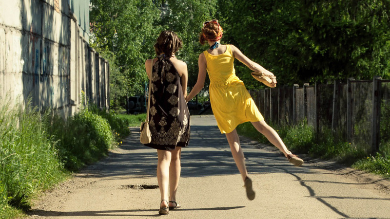 Deux femmes de dos marchent dans la rue. Celle de droite sautent de côté.