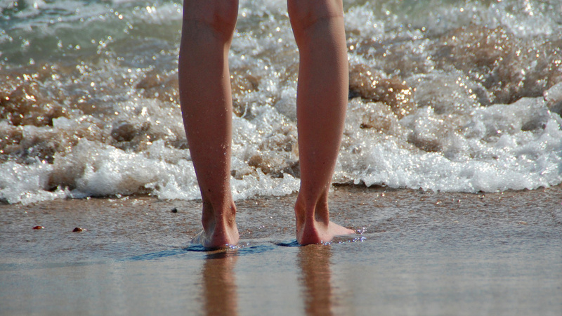 Pilzinfektionen, Fusspilz, Behandlung: Zwei Beine, die an einem Sandstrand am Wasser stehen